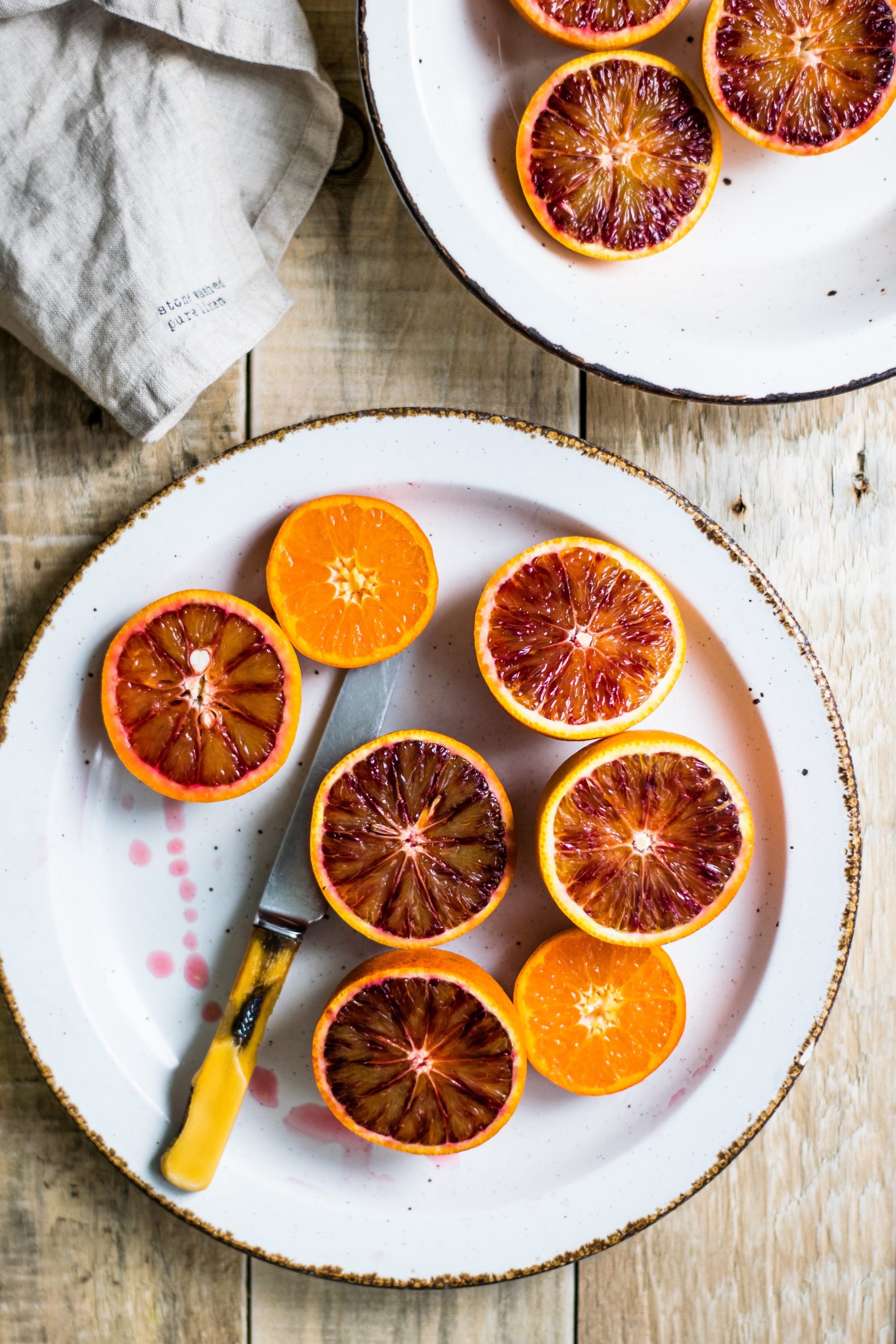Blood Oranges sliced in half on a white plate. The knife is laying between oranges on the plate, with juice around it.
