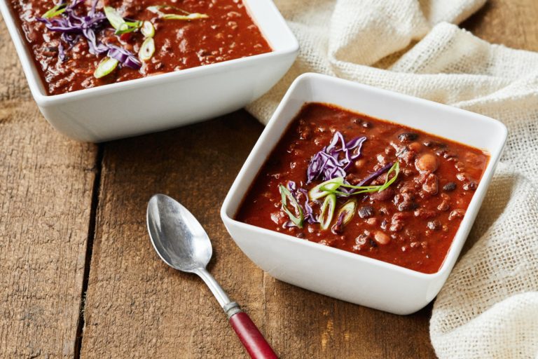 photo of 2 white square bowls of chili. There is a silver spoon with a red handle next to a bowl.