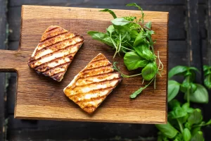 Grilled halloumi on a wooden cutting board with some fresh herbs